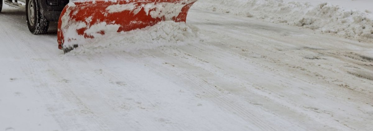 white truck with a red plow driving through snow - Spade Landscaping commercial snow plowing services